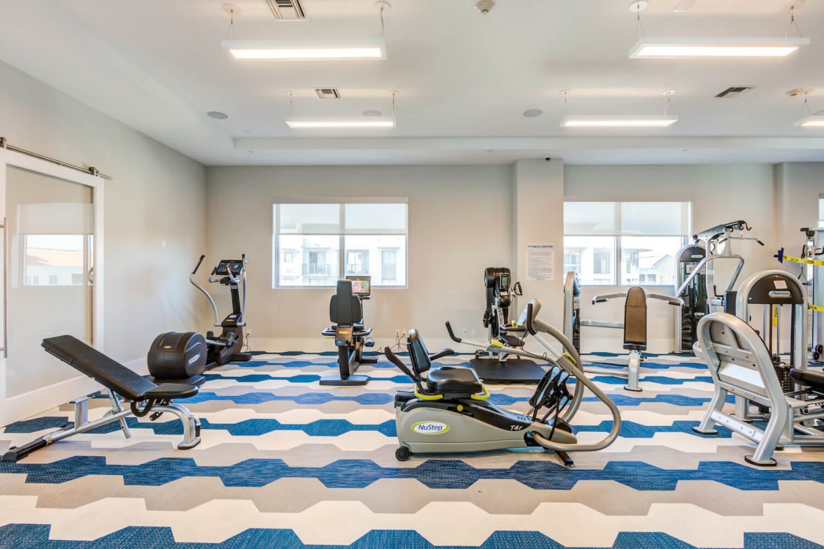 A modern gym with various exercise equipment and a patterned floor.