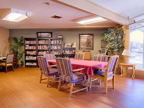A cozy dining area with a table and chairs surrounded by bookshelves and indoor plants.