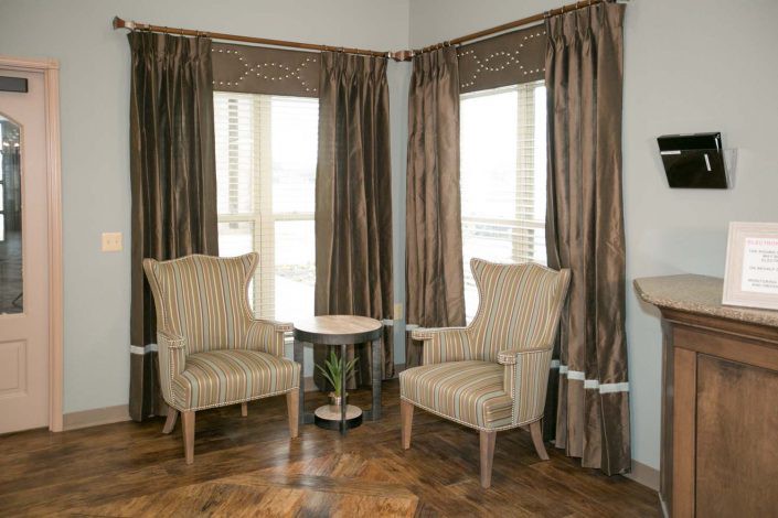 A cozy corner with two armchairs and a small table beside large windows with curtains.