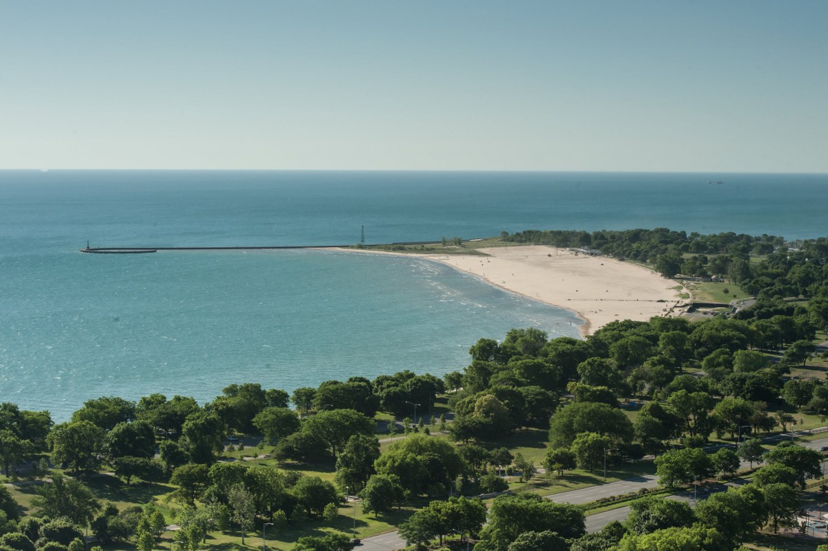 A scenic view of a coastline with a sandy beach and lush green trees overlooking the ocean.