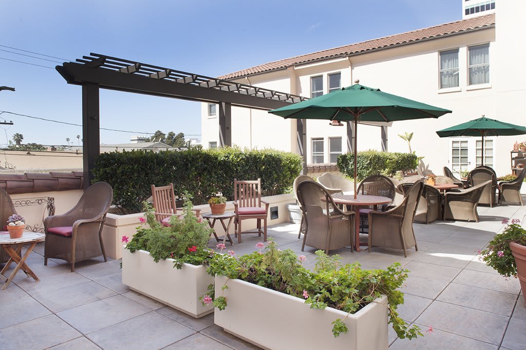 A cozy outdoor patio featuring wicker chairs, tables with umbrellas, and decorative planters on a sunny day.