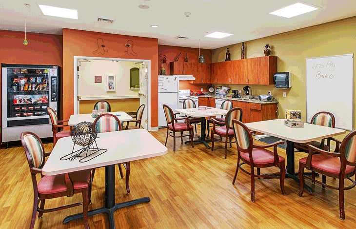 A communal dining and kitchen area with tables, chairs, and wooden flooring.