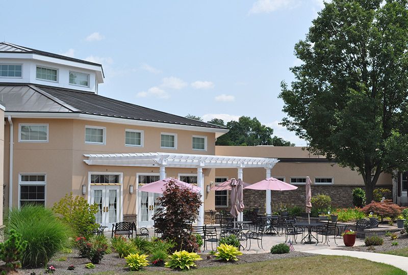 A patio area with pink umbrellas, surrounded by landscaped gardens and a building in the background.