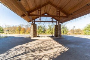 A wooden pavilion with a vaulted ceiling, surrounded by greenery and open space.