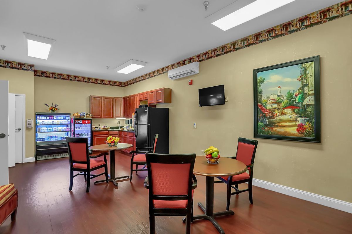 A cozy kitchenette with tables and chairs, featuring a fridge, television, and a decorative painting.