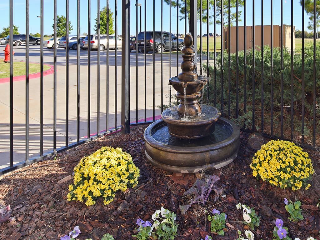 A decorative garden fountain surrounded by colorful flowers near an iron fence.