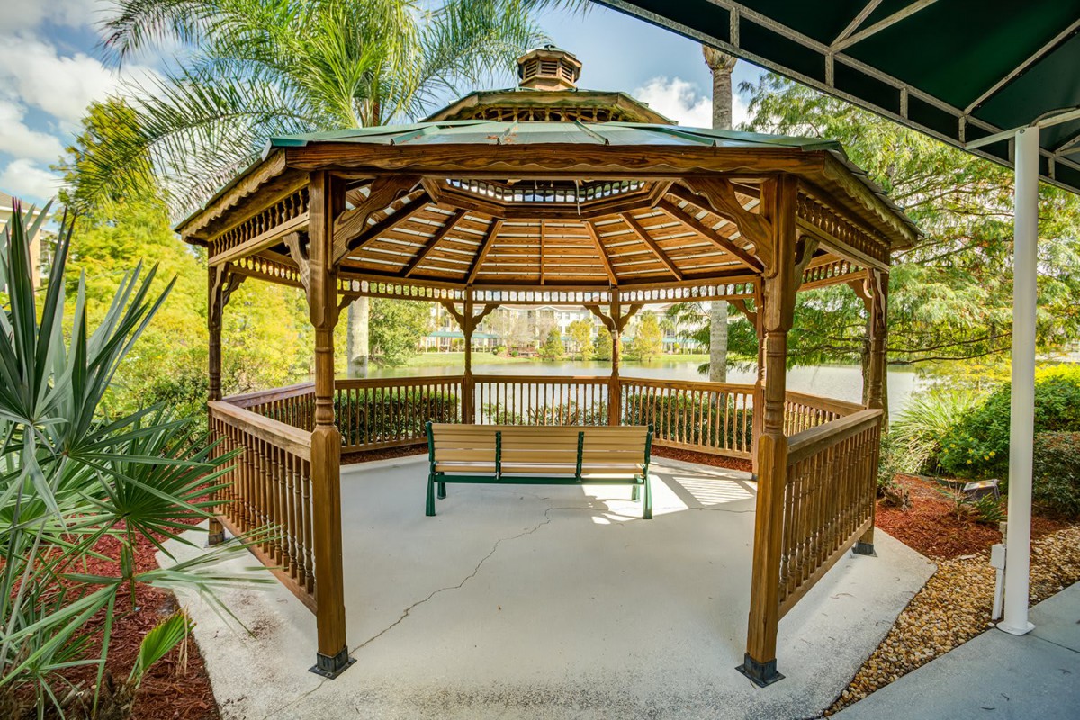 A wooden gazebo with a bench in a garden setting surrounded by palm trees.
