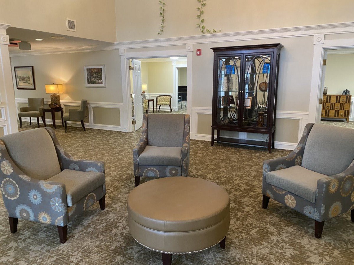 A cozy living room area with comfortable chairs, a round ottoman, and a wooden cabinet.