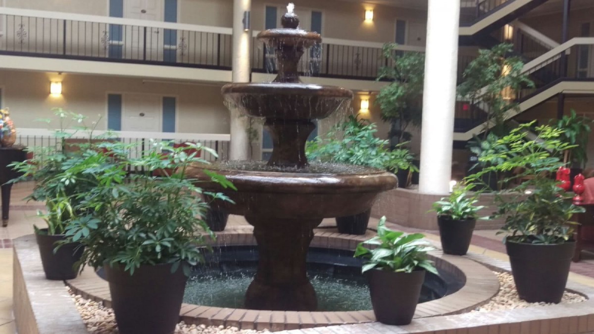 A multi-tiered fountain in an indoor atrium surrounded by potted plants.