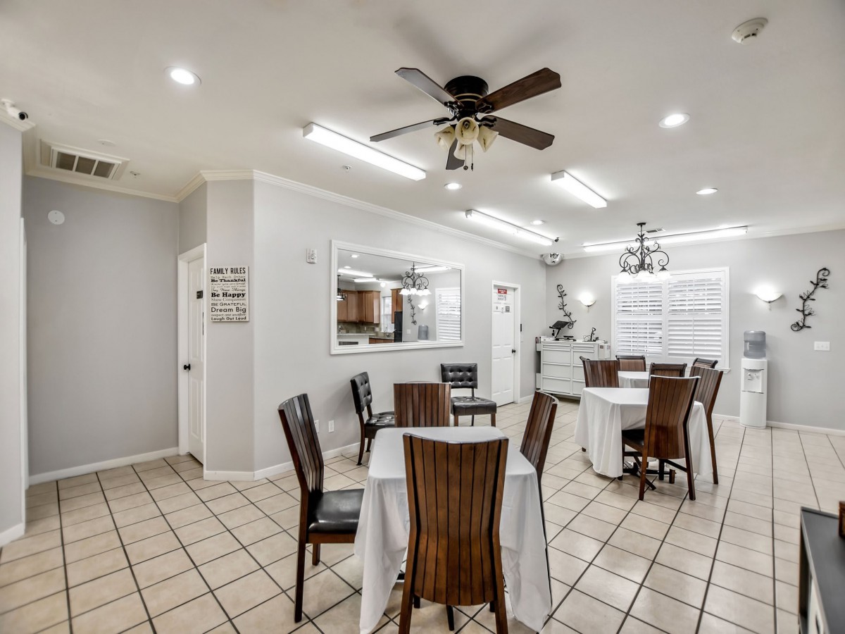 A cozy dining area with neatly arranged tables and chairs, featuring a ceiling fan and bright lighting.
