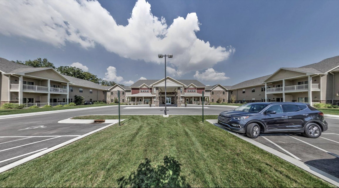 A wide view of a building with a parking lot and cars, set against a cloudy sky.