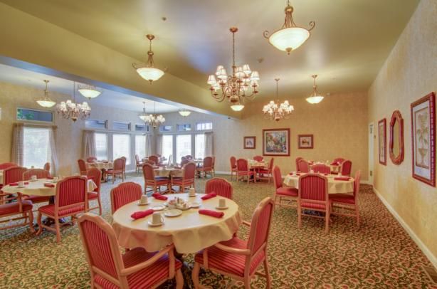 A spacious dining room with elegant chandeliers and red upholstered chairs.