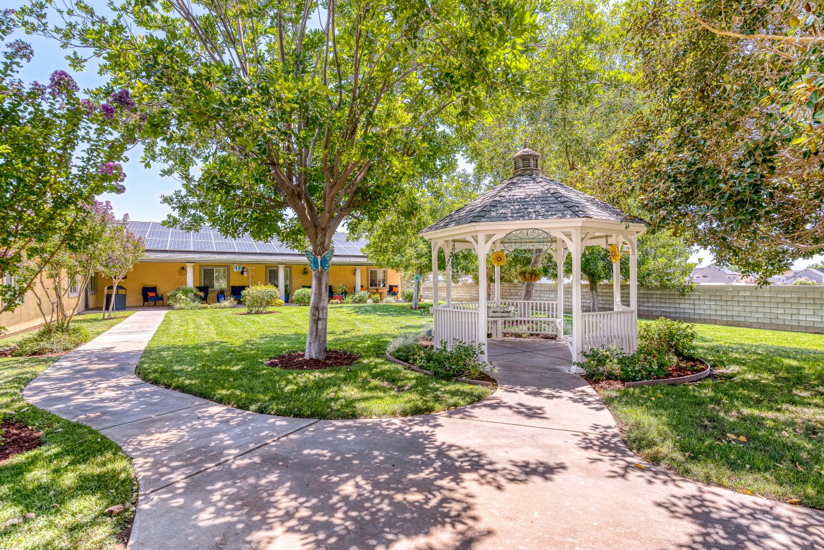 A peaceful garden featuring a white gazebo surrounded by lush greenery and winding pathways.