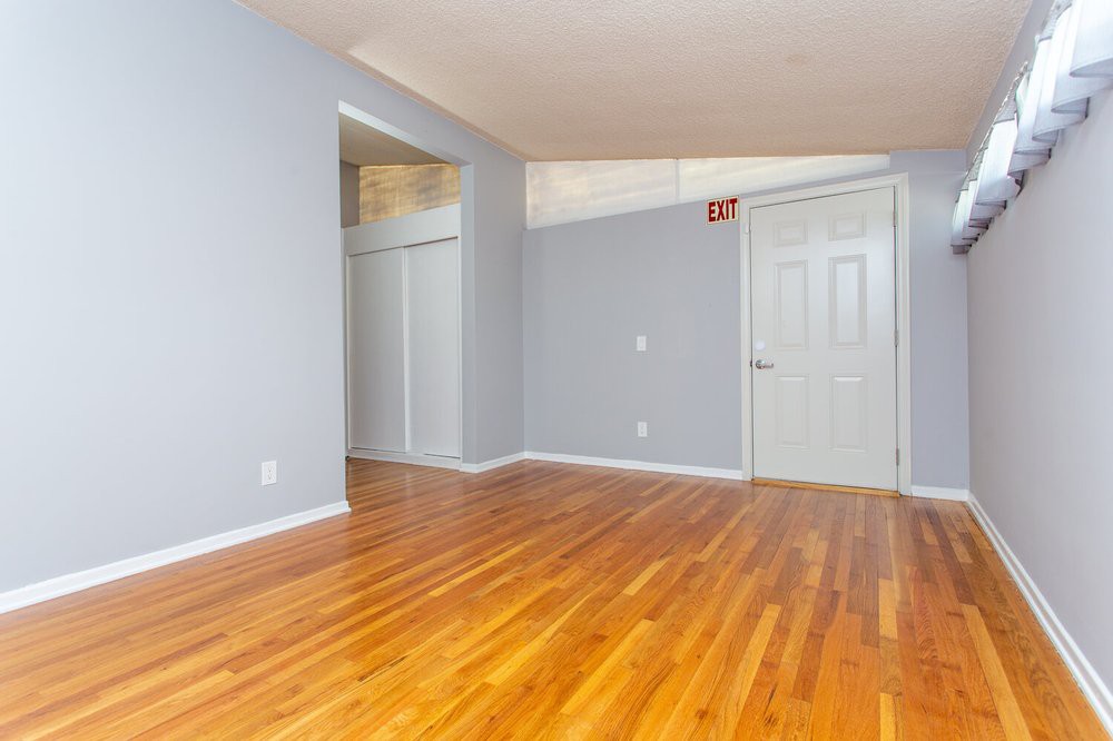 An empty room with light blue walls and polished hardwood flooring, featuring a closed door and a small closet.