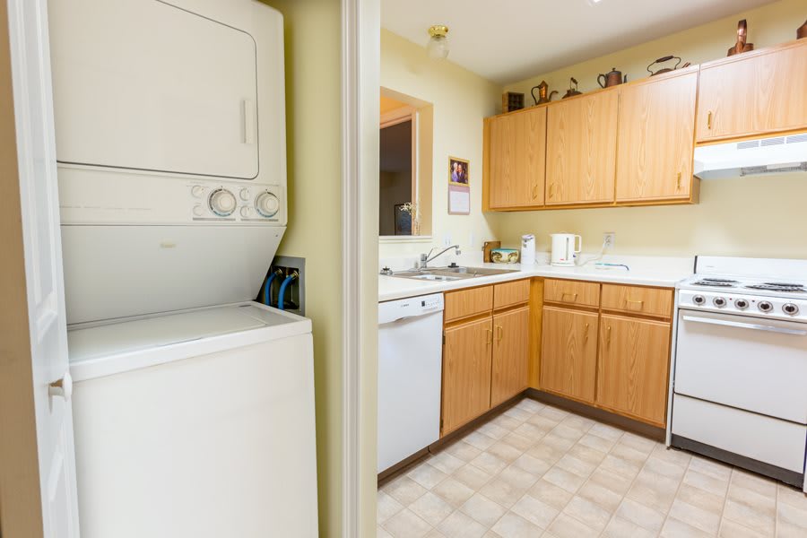 A cozy kitchen with wooden cabinets and a stacked washer and dryer unit in a nearby laundry area.