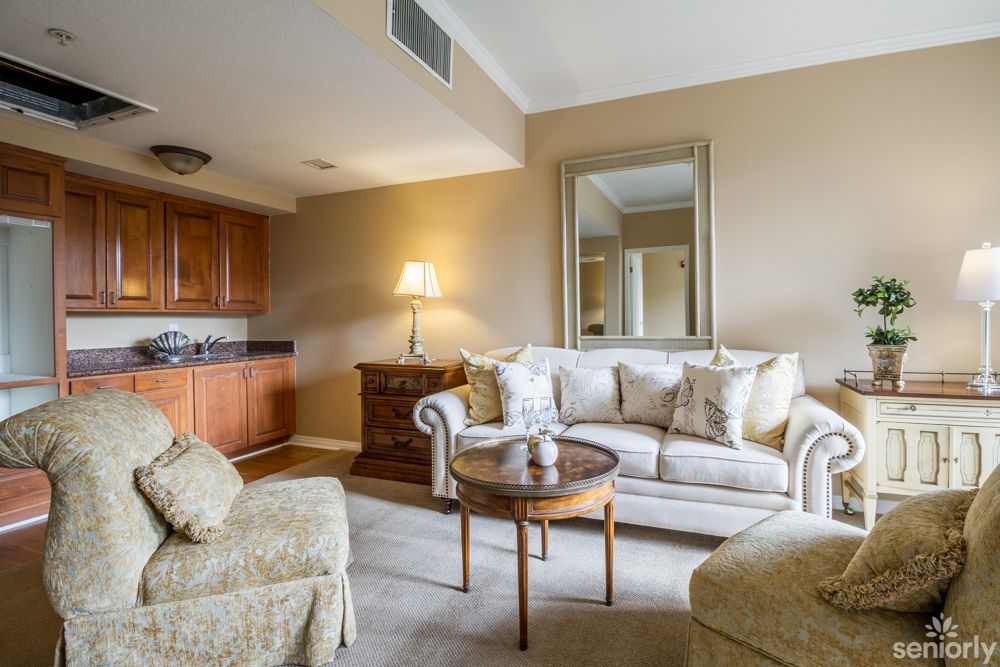 A cozy living room with a sofa, armchair, and wooden furniture, featuring a large mirror on the wall.