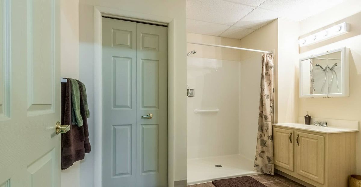 A bathroom with a shower area, a closed door, and a towel hanging on the wall.