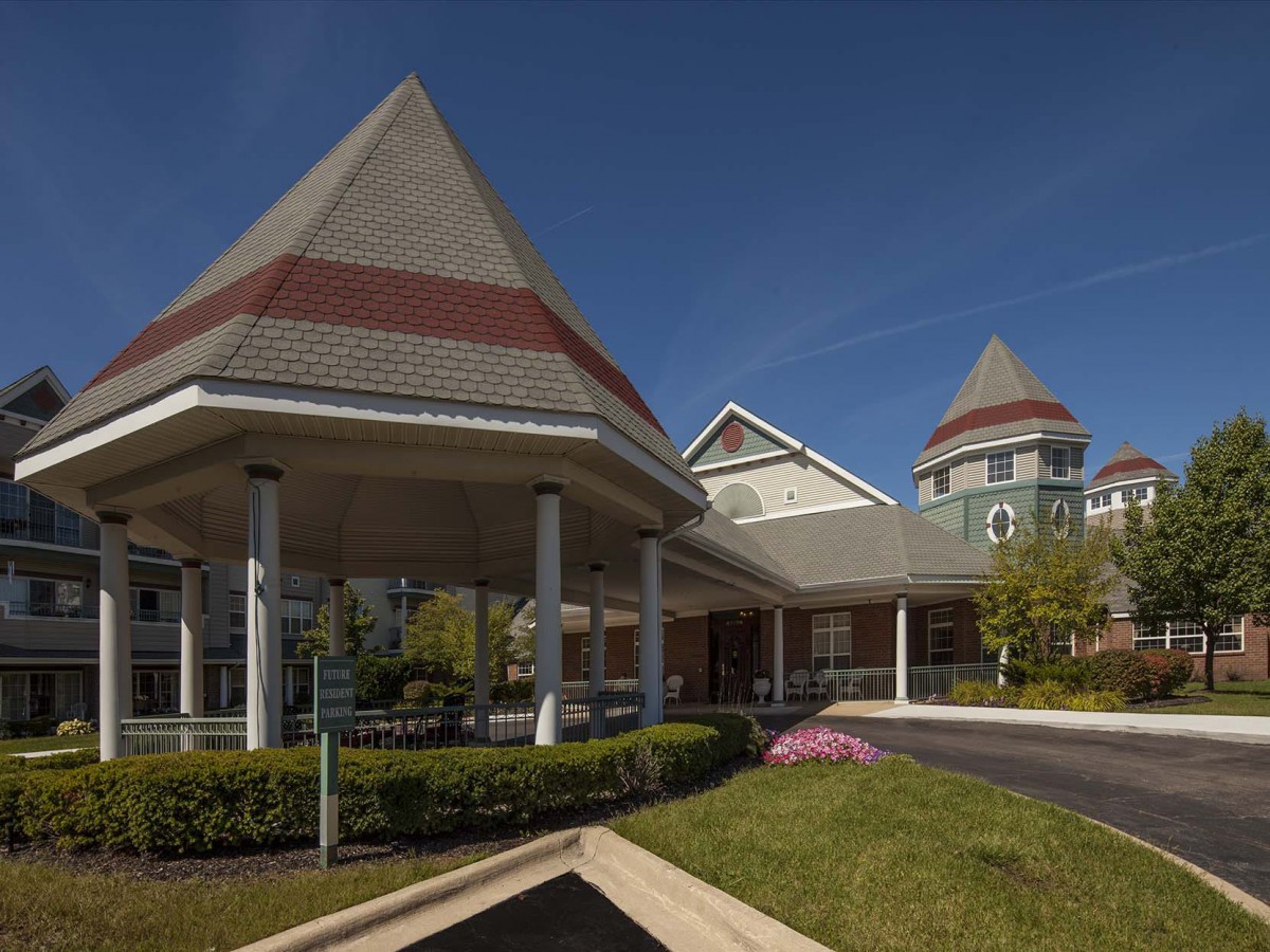 A scenic view of a building entrance with landscaped greenery and unique architectural features under a clear blue sky.