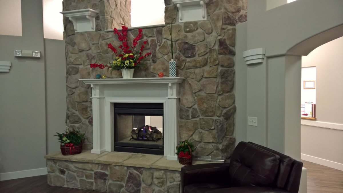A cozy indoor setting featuring a stone fireplace with decorative flowers on the mantel and a couch nearby.