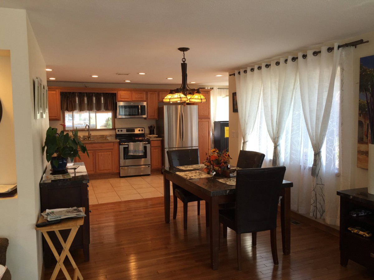 A modern open-concept kitchen and dining area featuring hardwood floors, stainless steel appliances, and a stylish chandelier.