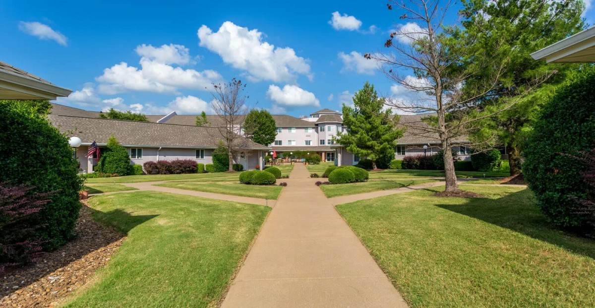 A scenic view of a building with a central pathway surrounded by lush greenery under a clear blue sky.