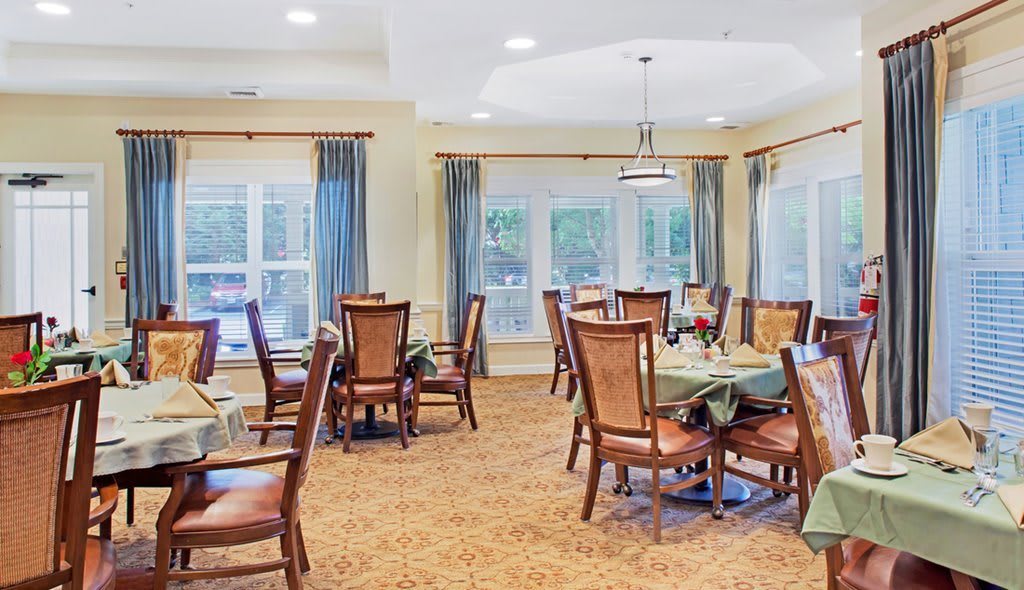 A bright dining room with elegant tables and chairs, surrounded by large windows and blue curtains.