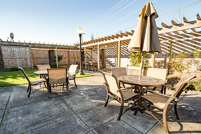 A sunny outdoor patio area with tables, chairs, and umbrellas under a wooden pergola.