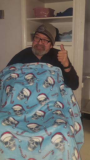 A man gives a thumbs up while wrapped in a cozy blanket featuring a fun skull design.