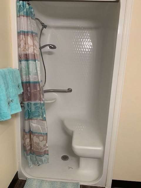 A small bathroom shower with a colorful curtain, grab bar, and bench seat.