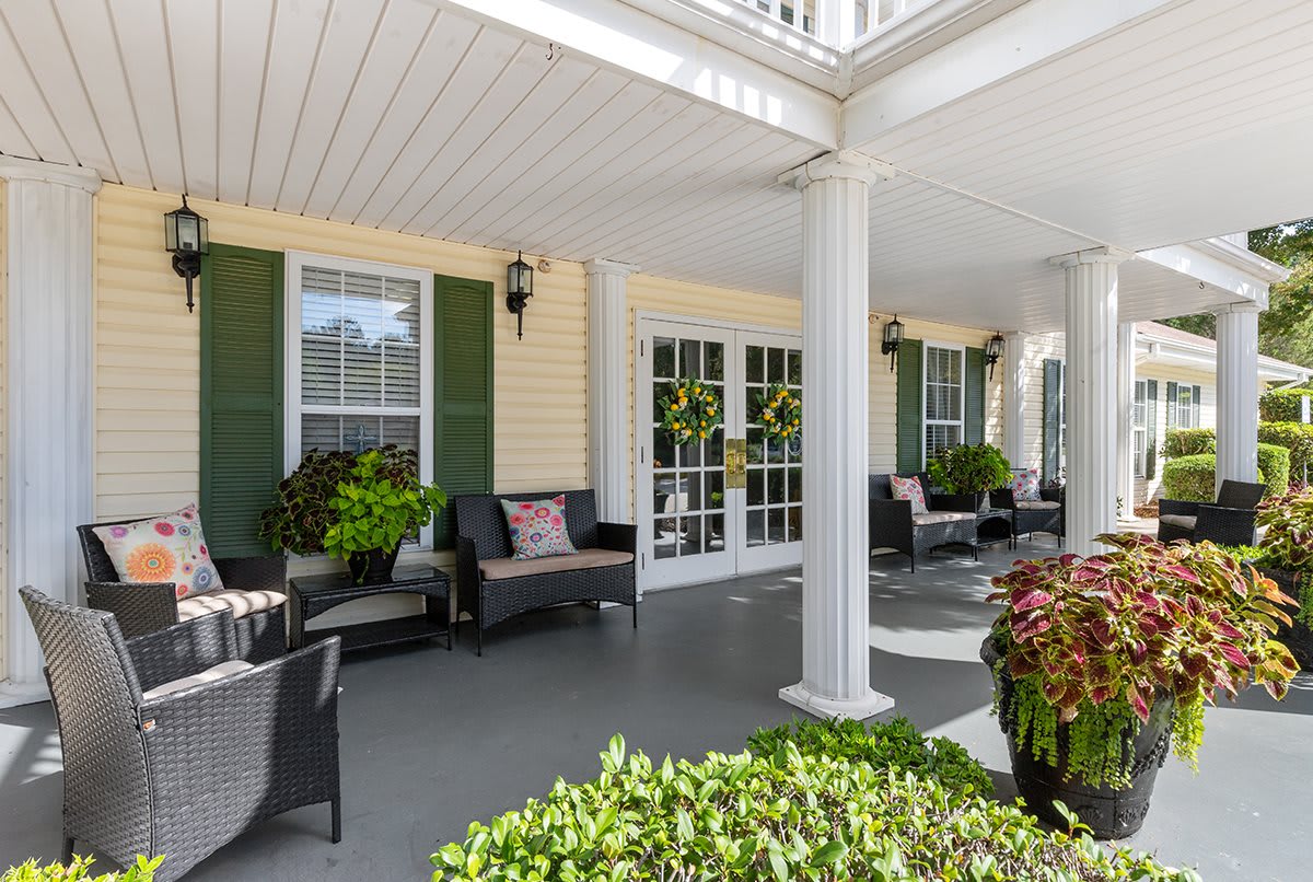 A spacious porch with comfortable seating and decorative plants, featuring classic columns and large windows.