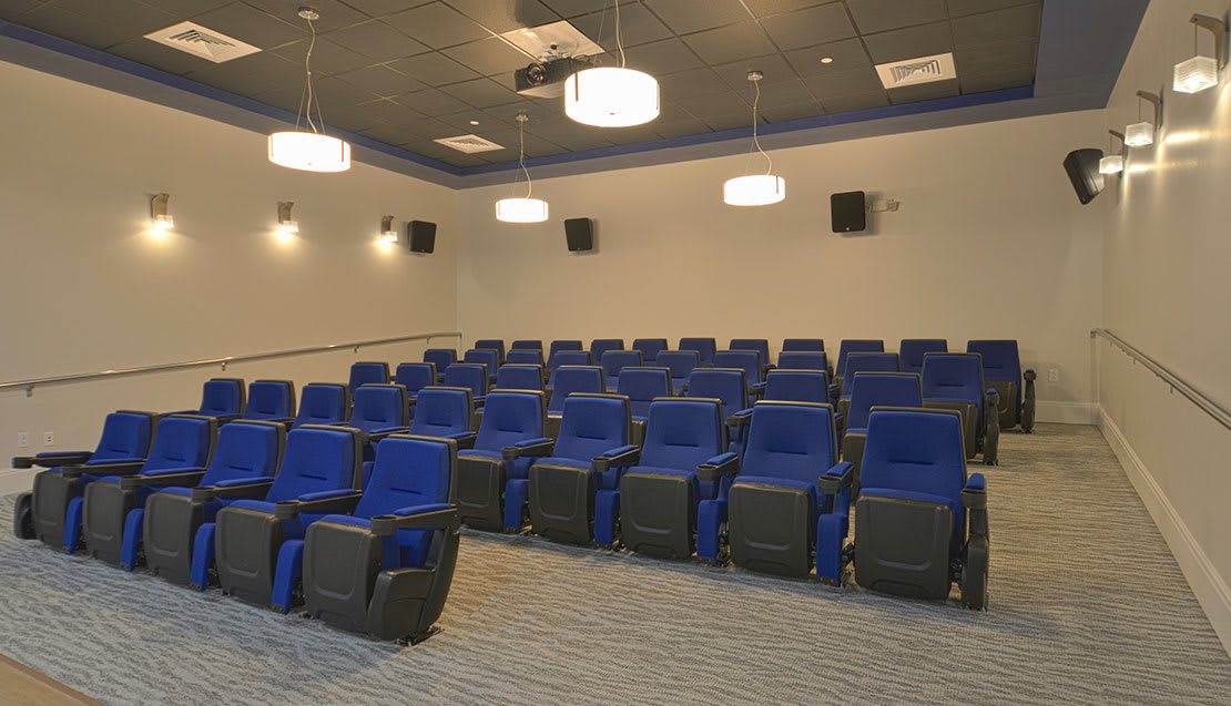 An empty theater room with rows of blue seats and overhead lighting.