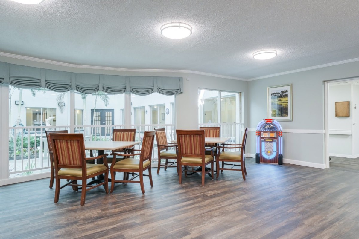 A cozy dining area with wooden tables and chairs, featuring large windows for natural lighting.