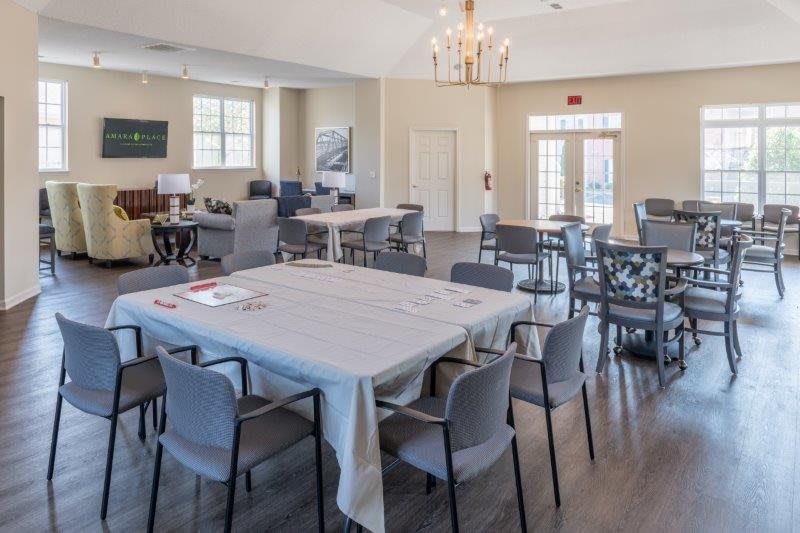 A spacious dining area with multiple tables and chairs, featuring a chandelier and hardwood floors.