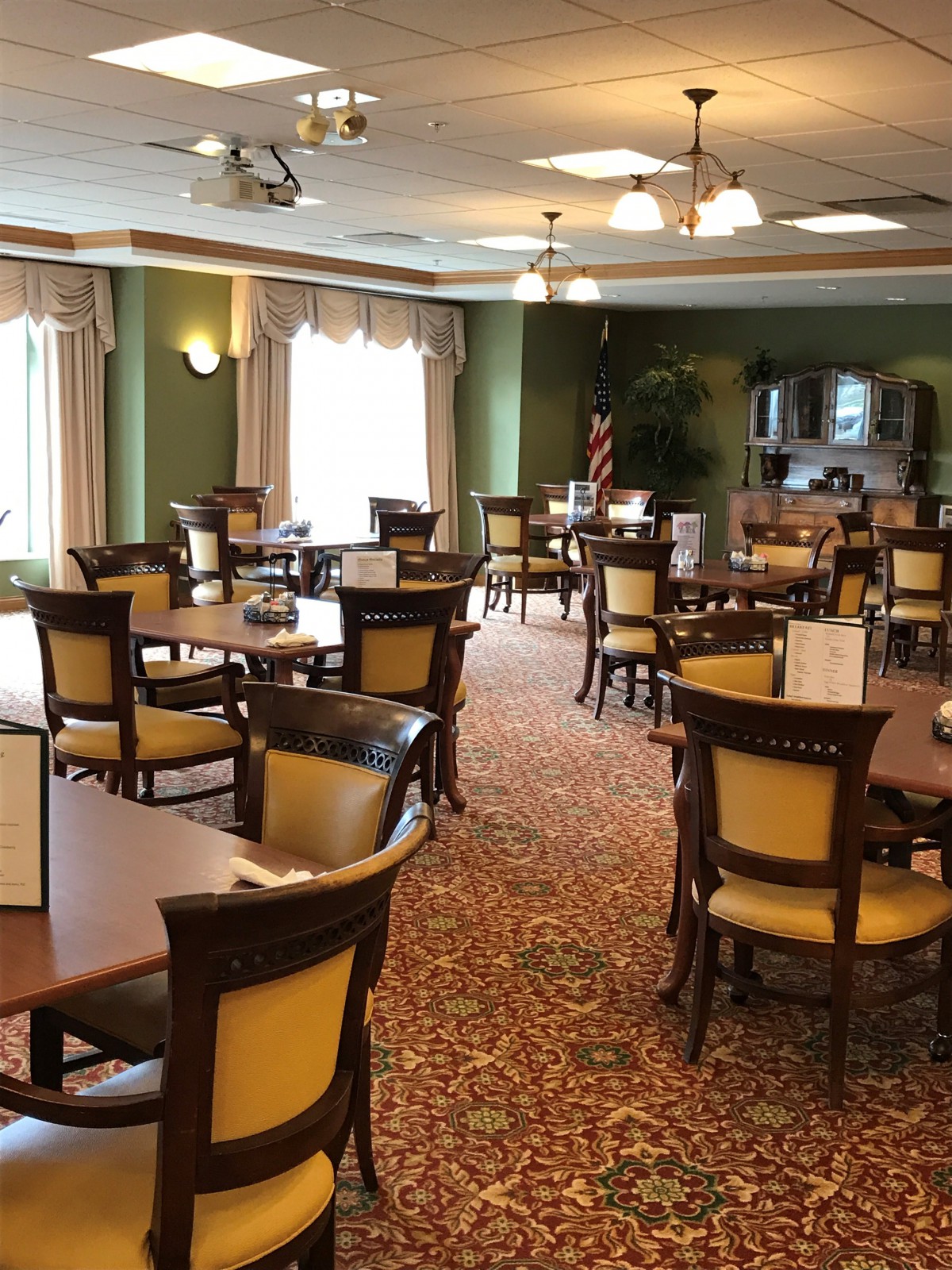 A well-lit dining area with neatly arranged tables and chairs, featuring elegant decor and carpeting.
