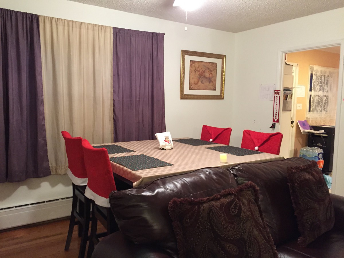 A cozy dining room with a large table, surrounded by red chairs and accented with mismatched curtains.