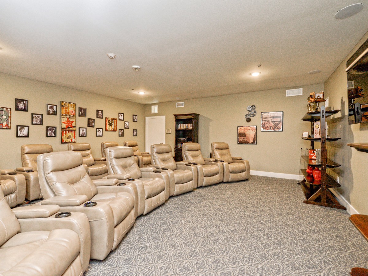 A cozy home theater room with rows of plush recliner chairs, decorated with movie posters on beige walls and a carpeted floor.