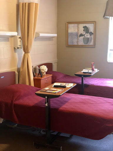 A patient room featuring two beds with side tables and a warm color scheme.