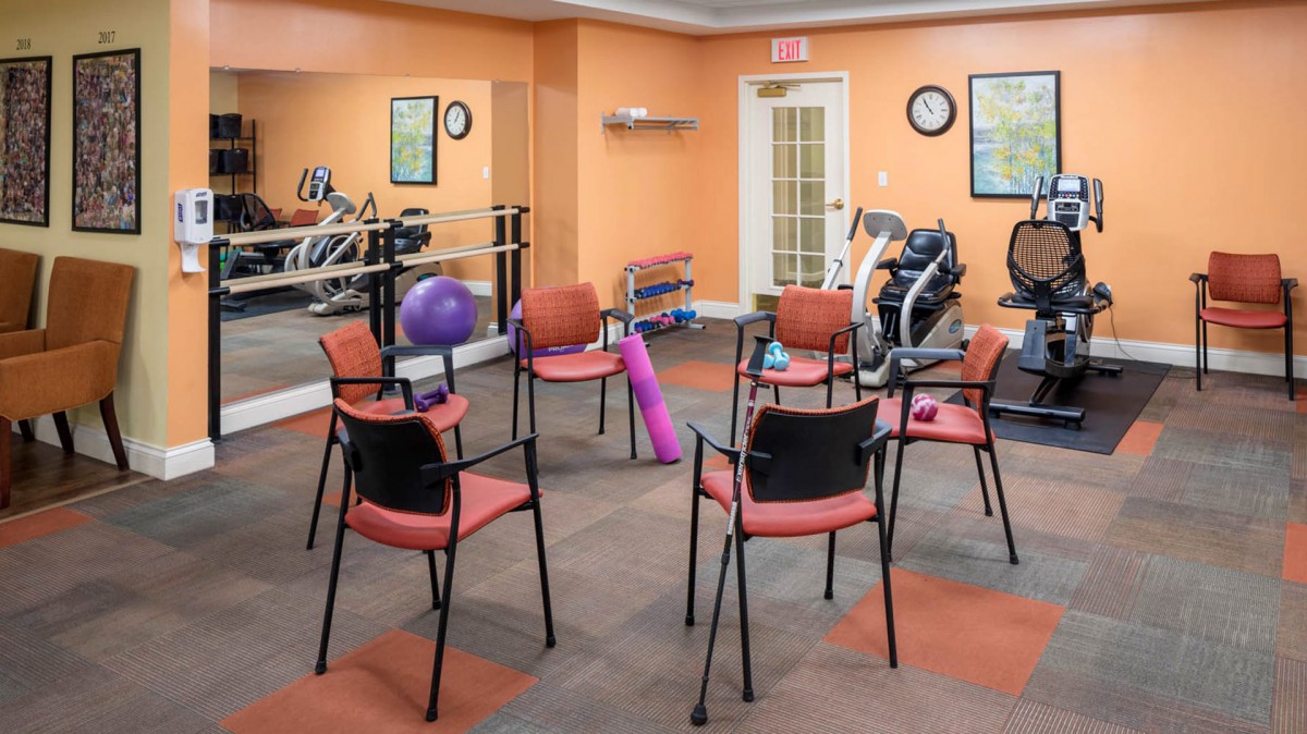 A fitness room with exercise equipment and chairs arranged in a circle for a group activity.
