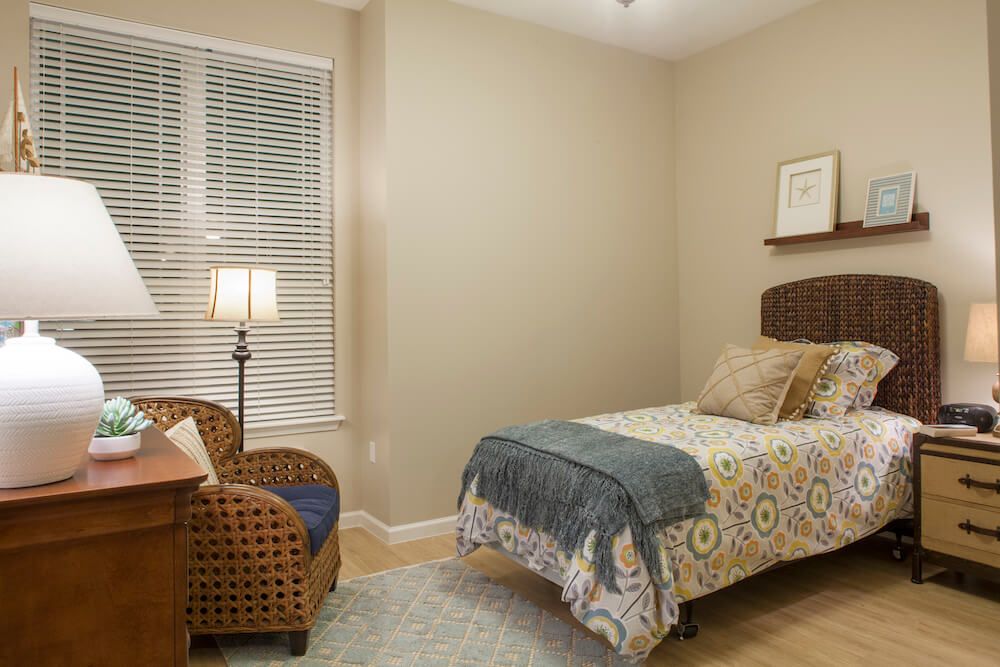 A cozy bedroom with a single bed, a wicker chair, and a floor lamp by the window.