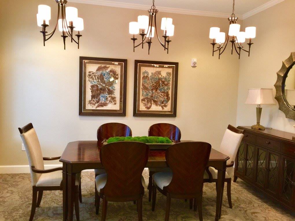 A well-decorated dining room with a wooden table, chairs, ornate chandeliers, and framed artwork on the walls.