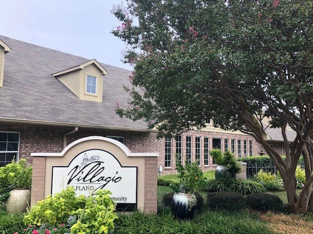 A residential building with a sign labeled 'Village Apartment Homes' surrounded by trees and greenery.