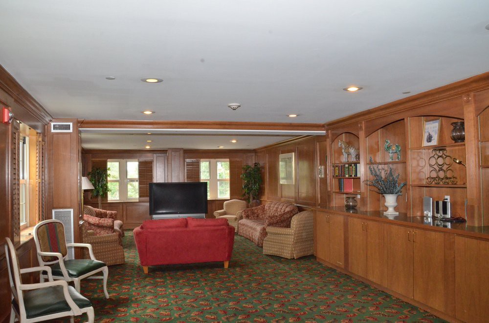 A cozy living room with wood paneling, featuring sofas, a television, and large windows.