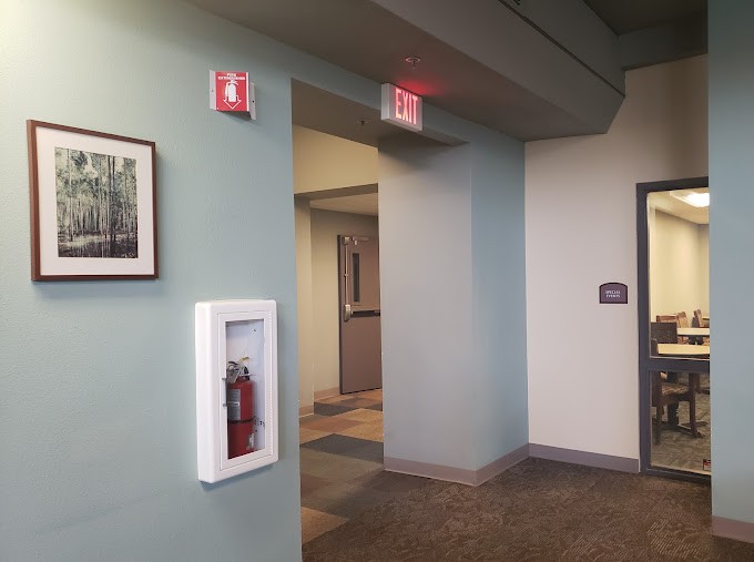 A hallway featuring a fire extinguisher, exit sign, and framed wall art.