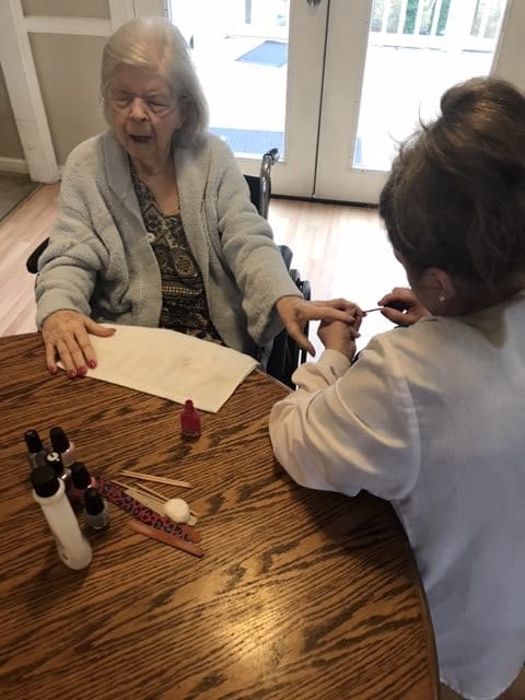 An elderly woman receives a manicure indoors, with nail polish bottles on the table.