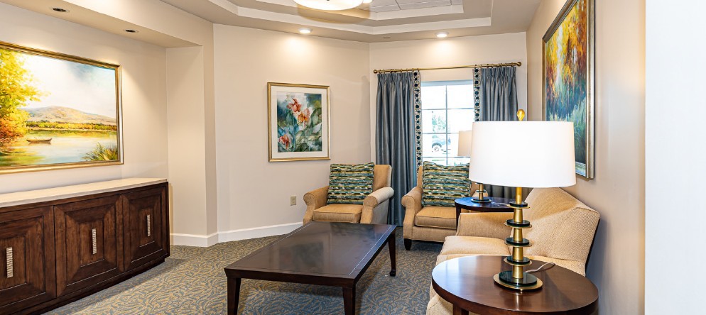 A cozy living room with comfortable chairs, a coffee table, and decorative elements like curtains and a framed painting.