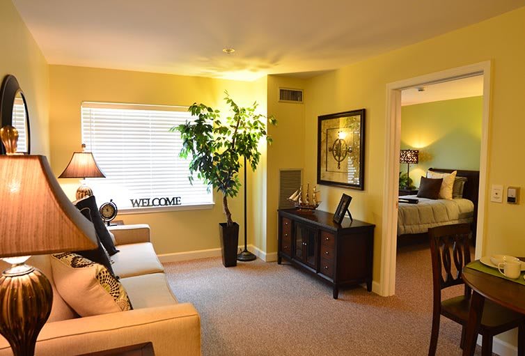 A cozy living room with warm lighting, featuring a sofa, decorative plants, and artwork on the walls.