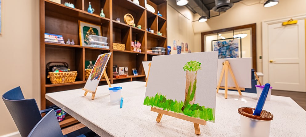 An art studio setup with an unfinished painting of a tree on an easel.