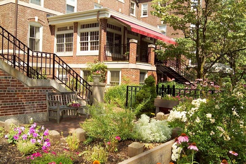 A lush garden with colorful flowers and outdoor seating in front of a charming brick building.