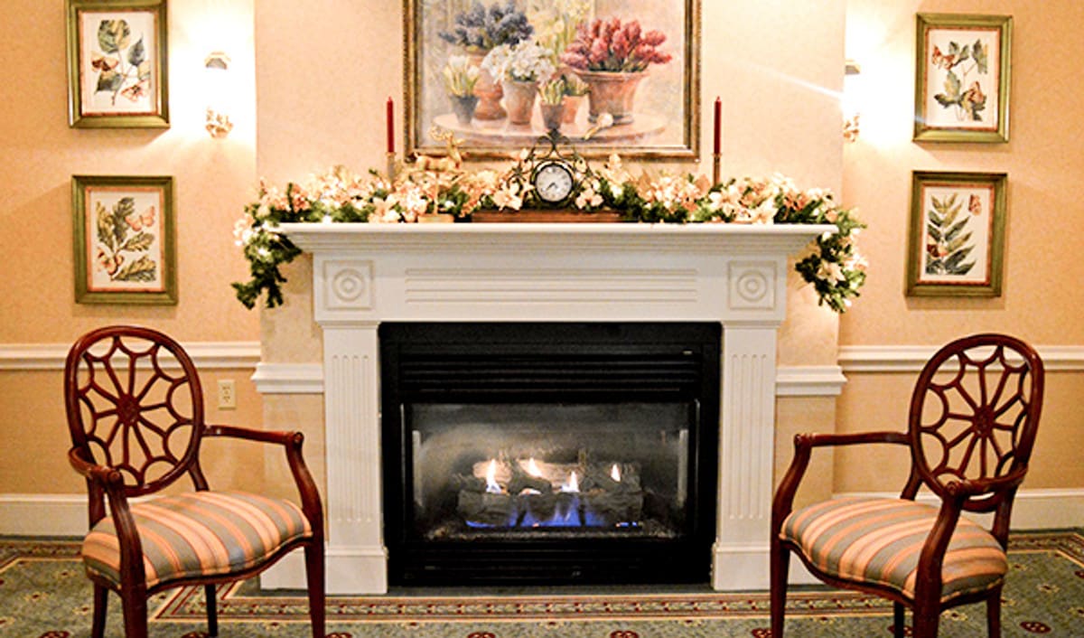 A cozy interior setting featuring a fireplace with floral decorations and chairs on either side.