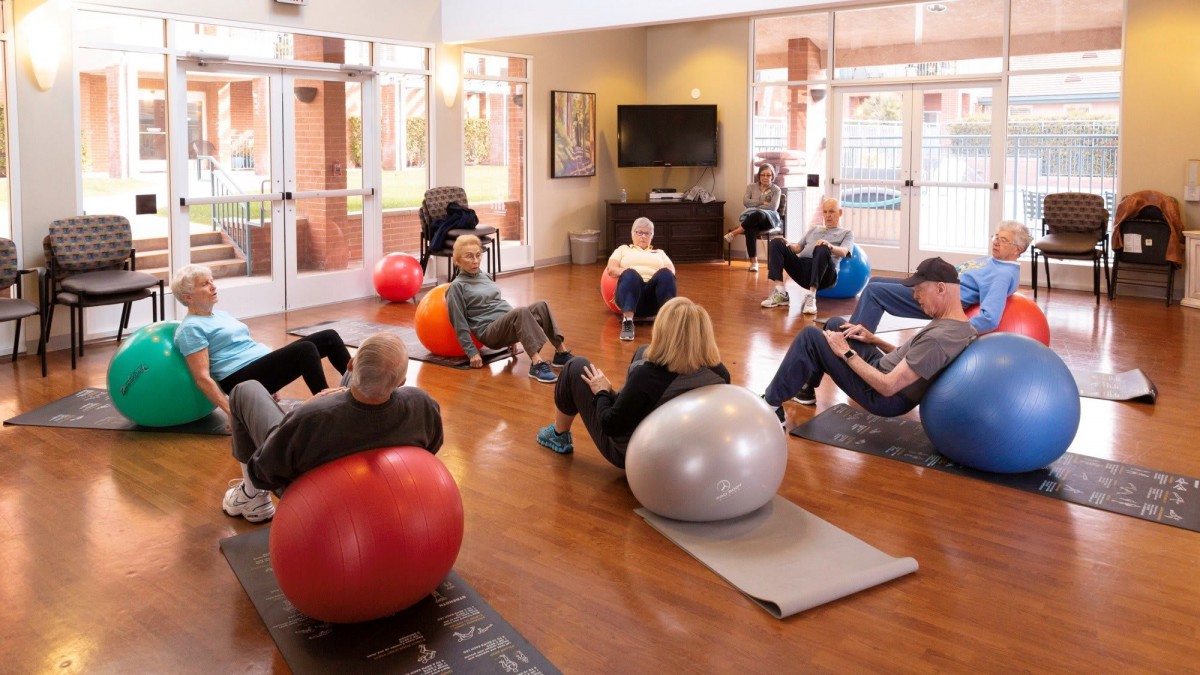 A group of people participating in an indoor fitness class using yoga balls.